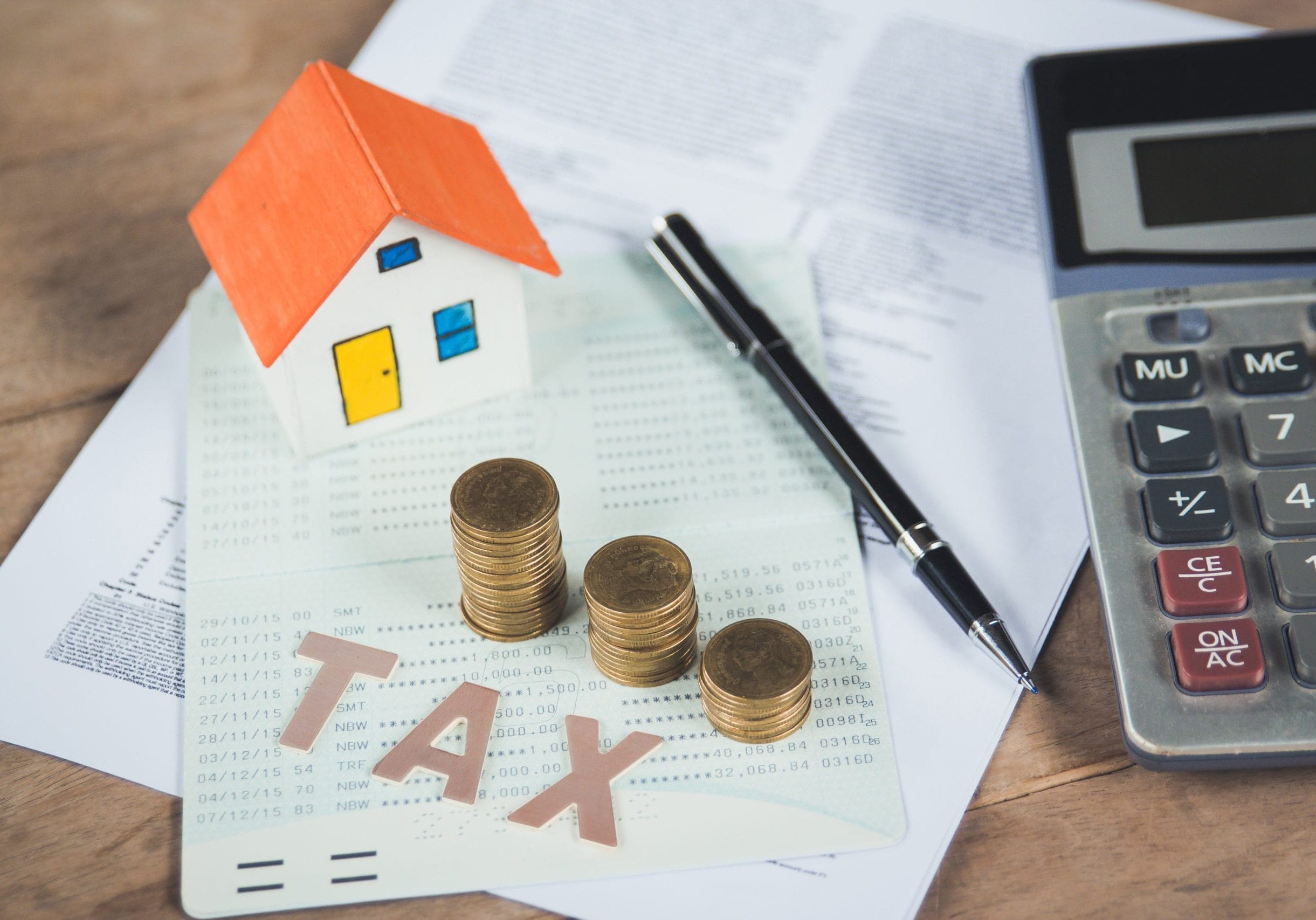 Model house with tax words,money,calculator and tax papers. Tax words written on table with calculator,pen, miniature house with money and tax papers.