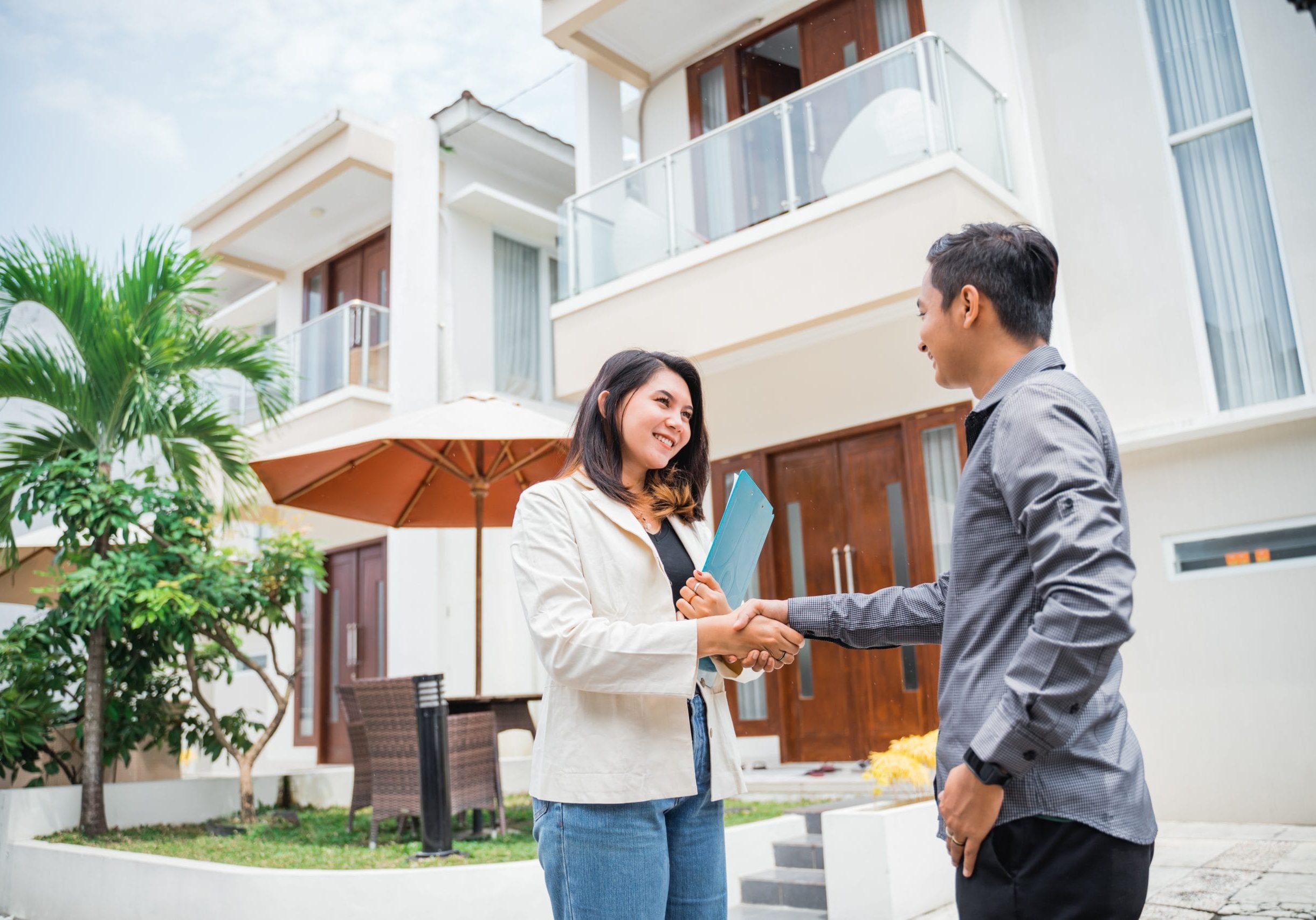 Asian female real estate agent shakes hands with prospective buyers in a residential background
