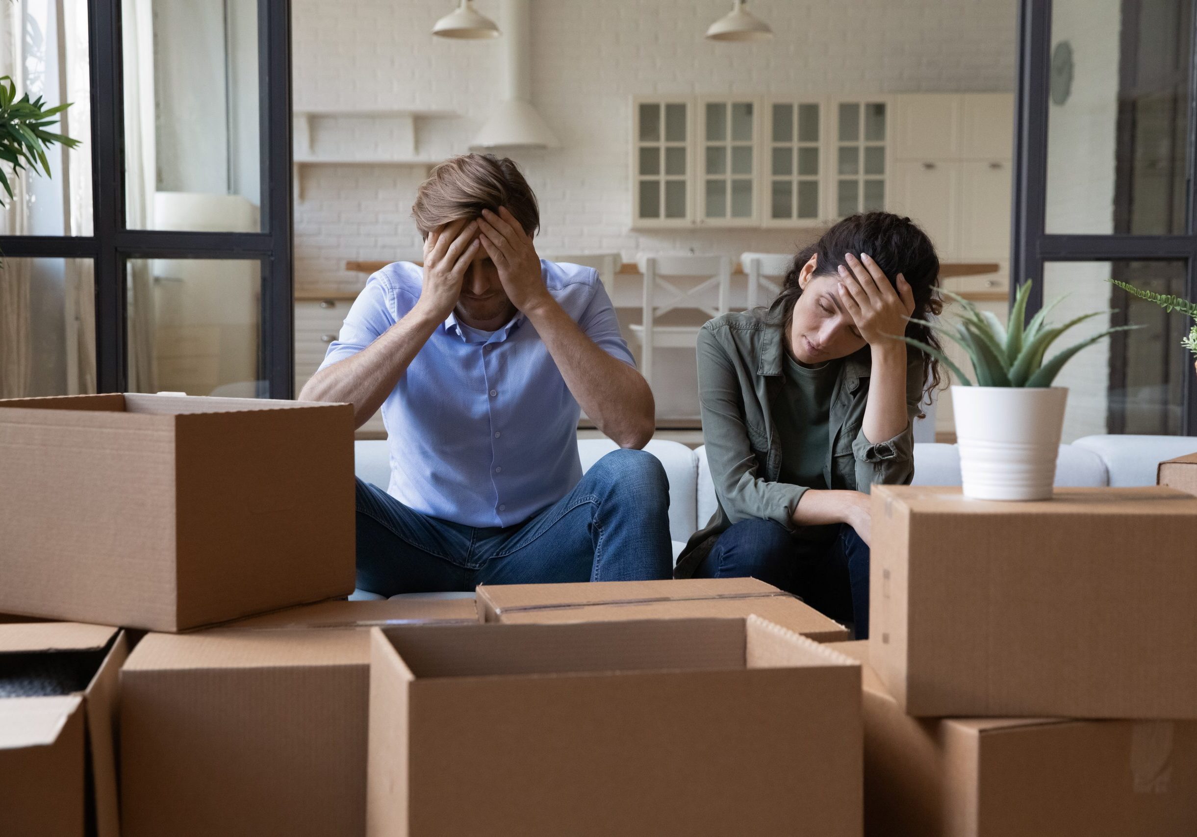 Exhausted young couple sit rest on sofa in living room near heap of cardboard boxes feel unmotivated to unpack their belongings. Financial problem, debt and eviction, hard long relocation day concept