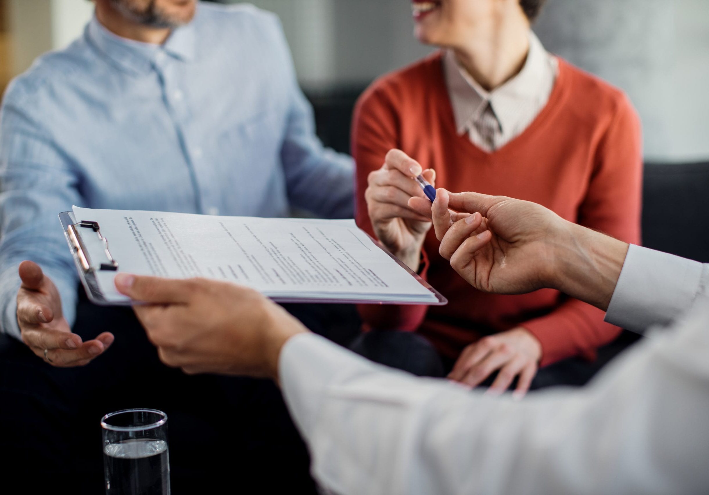 Close-up of woman signing an agreement with insurance agent while being on a meeting with her husband.